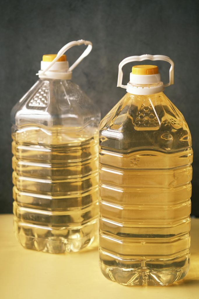 Two large recyclable plastic bottles filled with cooking oil on a yellow surface.